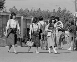 現在のように、インターネットや携帯電話のない時代。学生たちは、まず掲示板で休講情報などを確認してから、キャンパスライフをおくります。女子学生のスカートの丈やヘアスタイルなどが当時の流行を表しています。 掲示門前での女子学生